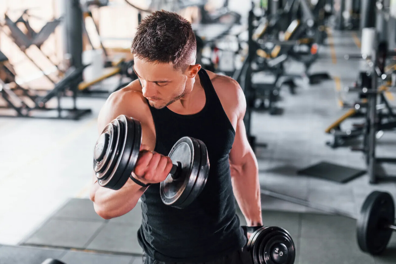 Liting dumbbells. Young sportive strong man in black wear have workout day in gym.; Shutterstock ID 1779955331